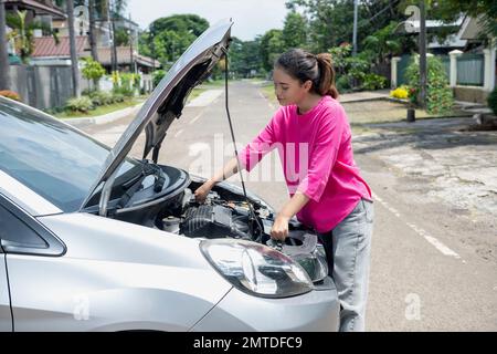 Eine asiatische Frau öffnet die Motorhaube und sucht nach einem störenden Auto, das neben der Straße steht Stockfoto