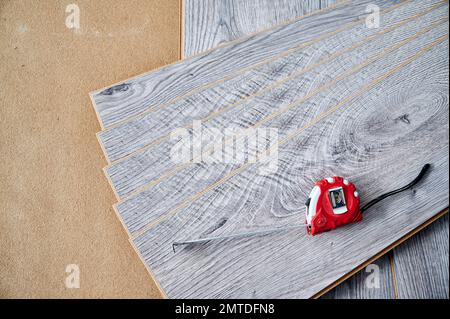 Maßband auf Holzböden für Hausrenovierungs-, Bauarbeiten- und Innenausbau. Maßband auf Proben von Laminatplatten mit Muster und Holzstruktur für Bodenbeläge. Stockfoto