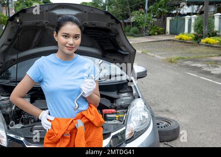 Asiatische Autotechnikerin in Uniform, die den Motor auf der Straße überprüft Stockfoto