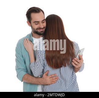 Ein Mann, der sich für ein Smartphone interessiert, während er seine Freundin auf weißem Hintergrund umarmt. Beziehungsprobleme Stockfoto