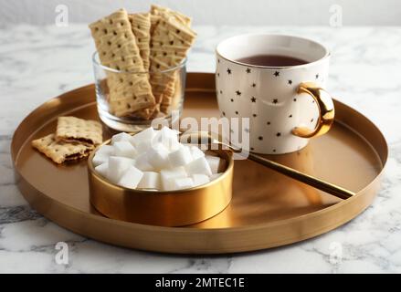 Raffinierte Zuckerwürfel in der Schüssel und aromatischer Tee auf einem weißen Marmortisch Stockfoto