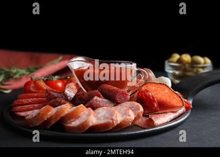 Verschiedene Wurstsorten mit Sauce auf schwarzem Tisch Stockfoto