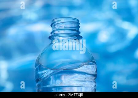 Nahaufnahme einer mit Wasser gefüllten Kunststoffflasche auf blauem Wasserhintergrund mit Lichtreflexionen Stockfoto