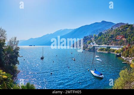 Wunderschöner Hafen am Lago Maggiore mit verankerten Yachten, kleinen Booten und Dingis, umgeben von blauen, trüben Bergen, Ascona, Schweiz Stockfoto