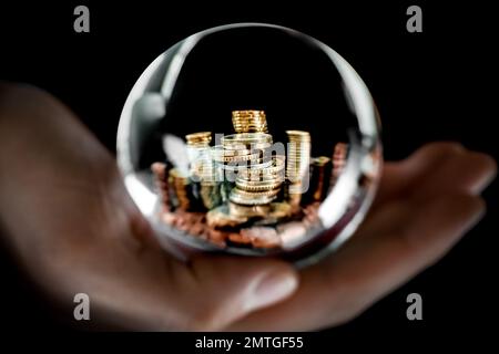 Symbolisches Bild von mehreren metallischen europäischen Geldmünzen, die in Stapeln gestapelt sind, mit einem Kopierraum auf der Oberseite, durch eine transparente Glaskugel zu sehen. Stockfoto