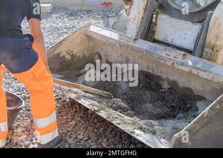 Auf der Baustelle kneten Straßenarbeiter Zementmörtel in die Eimer eines Baggers Stockfoto