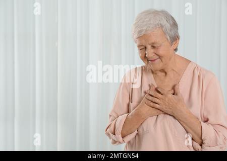 Dankbare ältere Frau mit Händen auf der Brust vor hellem Hintergrund. Platz für Text Stockfoto