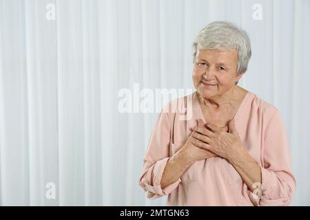 Dankbare ältere Frau mit Händen auf der Brust vor hellem Hintergrund. Platz für Text Stockfoto