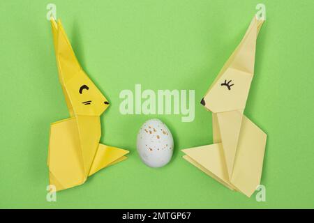 Oster-Origami - zwei Papierhasen und ein Ei mit grünem Hintergrund. Basteln für die Feiertage, machen Sie es selbst. Stockfoto