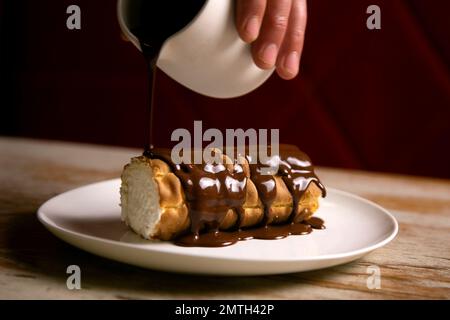 Schweizer Brötchen gefüllt mit Sahne und bedeckt mit dunkler Schokolade. Stockfoto