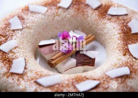 Klebriger Reis-Kokosnuss-Kuchen mit ein paar Blumen und frischer Kokosnuss in der Mitte. Stockfoto