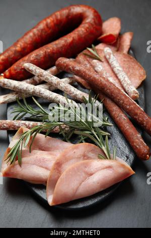 Verschiedene leckere Würstchen und Rosmarin auf schwarzem Tisch Stockfoto