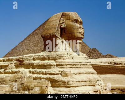 Skulptur der Großen Sphinx vor dem blauen Himmel. Profilansicht. Der Kopf, ein Teil des Körpers und die Spitze der antiken Pyramide über dem Rücken sind Vis Stockfoto