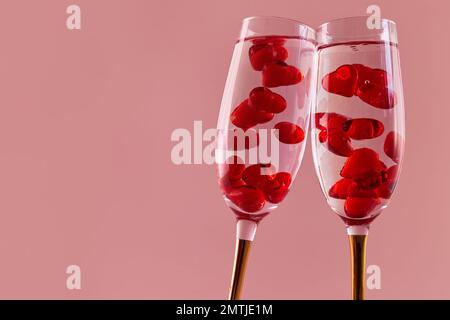 Alles Liebe zum Valentinstag. Zwei Gläser Champagner mit roten Herzen. Rosafarbener Hintergrund. Stockfoto