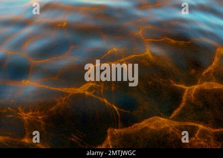 Abstraktes Foto der Textur der Reflexion von Licht von der Oberfläche der Wasserwellen des Flusses vom Himmel in hellen Gelbtönen. Stockfoto