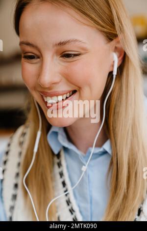 Blonde weiße Frau, die Musik hört, während sie im Café drinnen sitzt Stockfoto