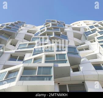 Sie blickt nach oben entlang der weißen, gewellten Fassade. Prospect Place Battersea Power Station Frank Gehry, London, Vereinigtes Königreich. Architekt: Frank Gehry, 2022 Stockfoto