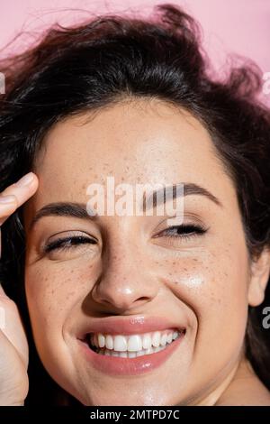 Nahaufnahme einer positiven Frau mit Sommersprossen, die die Haut berührt, isoliert auf einem pinkfarbenen Stockbild Stockfoto