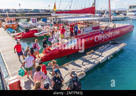 Touristen, die an Bord des Obycat Experience Katamarans gehen, fahren im Hafen von Caleta de Fuste an der Ostküste der Kanarischen Insel Fuerteventura, Spanien Stockfoto