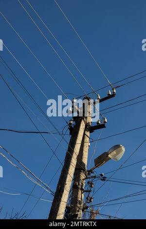 Elektrische Kabel hängen an einem Stab mit einer Lampe, die von unten auf einem Hintergrund mit blauem Himmel fotografiert wurde. Stockfoto