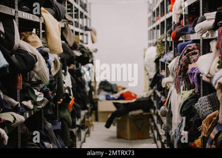 Humanitäre Hilfe Station, im Inneren des Industrielagers mit gebrauchter Kleidung für die Armen, Flüchtlinge, schutzbedürftige Menschen. Regale, Kleiderreihen Stockfoto