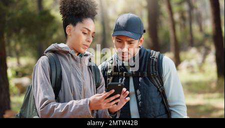 Wandern, Smartphone und Reisepaar mit Standortsuche, Online-Reiseführer oder Naturreiseplanung zusammen in einem Wald auf 5G Netzwerk. Rucksack Stockfoto