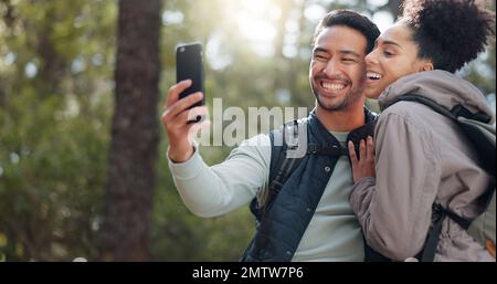 Wandern, Spazierengehen und ein junges Paar im Wald auf Abenteuern, Reisen und Erkundung der Natur. Asiatischer Mann und schwarze Frau, die wandern, spazieren gehen und Selfie machen Stockfoto