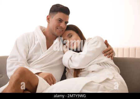 Glückliches Paar in Bademänteln auf dem Sofa zu Hause Stockfoto