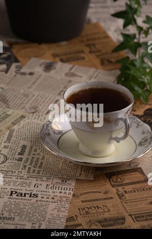 Fotografieren Sie eine alte Kaffeetasse und einen Zweig grüner Pflanzen vor dem Hintergrund alter Zeitungsausschnitte Stockfoto