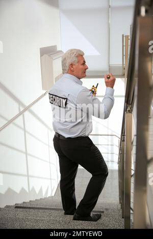 Professioneller Wachmann mit Taschenlampe auf Treppen im Innenbereich Stockfoto