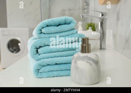 Stapel sauberer Handtücher und Seifenspender auf der Arbeitsfläche im Badezimmer Stockfoto