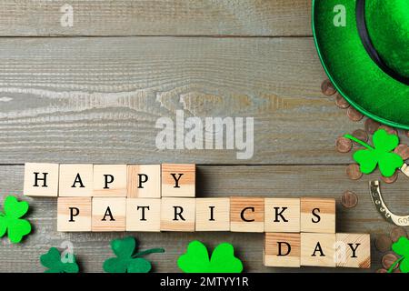 Holzwürfel mit Wörtern FRÖHLICHER St. PATRICK'S TAG, Hufeisen, Goldmünzen und Kleeblätter auf dem Tisch, flach liegend. Platz für Text Stockfoto