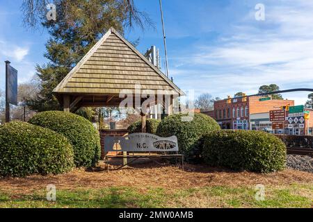 WAXHAW, NC, USA-28. JANUAR 2023: „Welcome to Waxhaw“-Stahlbank vor dem Pavillon mit Brunnen und Eimer. Sonniger, blauer Himmel. Stockfoto