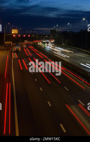 Der überhöhte Verkehr auf der Autobahn M42 während der abendlichen Hauptverkehrszeit hinterlässt aufgrund der langsamen Verschlusszeit und langen Belichtungszeiten helle Spuren und Streifen. Stockfoto