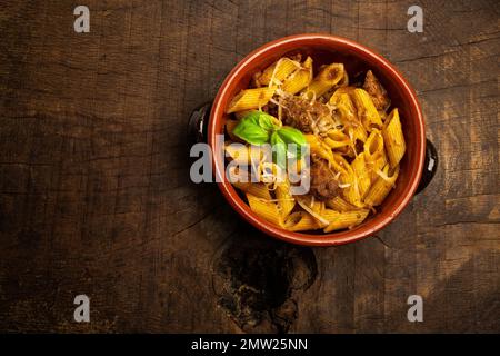 Frisch hausgemachtes Gulasch mit italienischer Penne Pasta in Terrakotta-Schüssel auf einem alten rustikalen Holztisch. Stockfoto