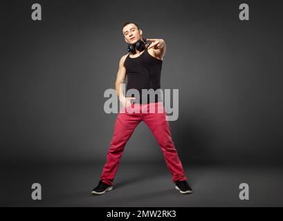 Ganzkörperporträt eines jungen selbstbewussten Mannes, der auf grauem Hintergrund posiert. Stockfoto