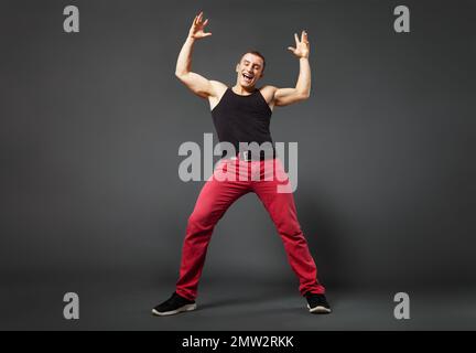Ganzkörperporträt eines jungen Mannes, der vor grauem Hintergrund tanzt. Niedriger und weitwinkliger Betrachtungseffekt. Stockfoto