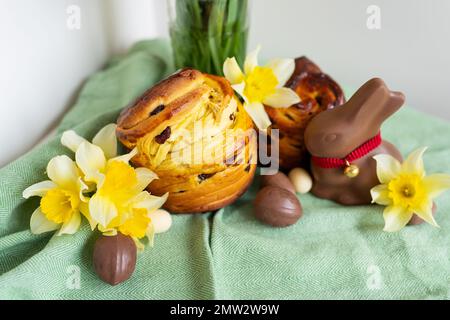 Hausgemachtes traditionelles Ostergebäck liegt auf einer grünen Serviette zusammen mit Narzissen, Kaninchen und Schokoladeneiern. Osterbacken und Dekoration Stockfoto