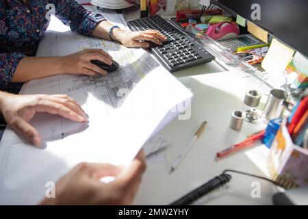 Hände von zwei Kollegen bei der Arbeit in einem technischen Büro, die am pc arbeiten und eine Zeichnung untersuchen. Stockfoto