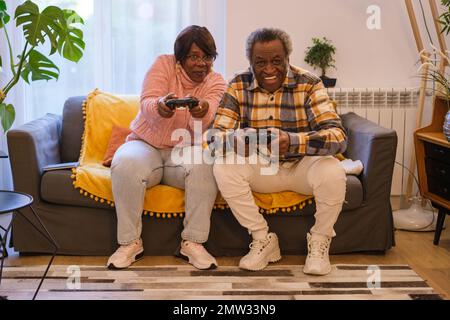 Seniorenpaar afrikanischer Abstammung mit Spielkonsole und Spaß mit neuen Technologien zu Hause. Konzept: Lernen, Ruhestand, Bindung Stockfoto