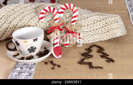 Eine Weihnachtstischszene mit einer leeren Tasse Kaffee, zwei dekorativen Zuckerstangen und einem Weihnachtsbaum aus Kaffeebohnen mit einem kleinen Weihnachtsmannmütze Stockfoto