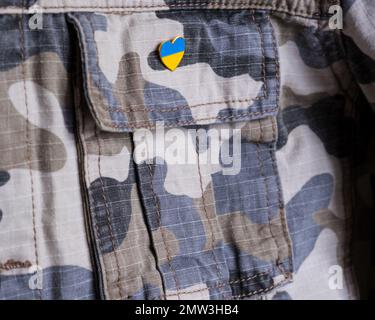 Metallabzeichen mit ukrainischer Flagge in Form eines Herzens auf Militärjacke. Unterstützung für die Ukraine. Krieg in der Ukraine. Ukrainisches Flaggenthema Stockfoto