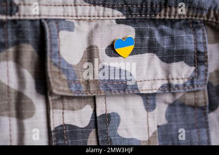 Metallabzeichen mit ukrainischer Flagge in Form eines Herzens auf Militärjacke. Unterstützung für die Ukraine. Krieg in der Ukraine. Ukrainisches Flaggenthema Stockfoto