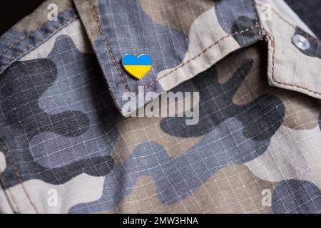 Metallabzeichen mit ukrainischer Flagge in Form eines Herzens auf Militärjacke. Unterstützung für die Ukraine. Krieg in der Ukraine. Ukrainisches Flaggenthema Stockfoto