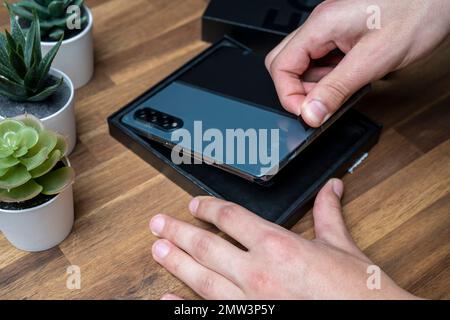 Samsung Galaxy Z Fold 4 in grau-grüner Farbe. Ein Mann packt das neue Handy aus. Stockfoto