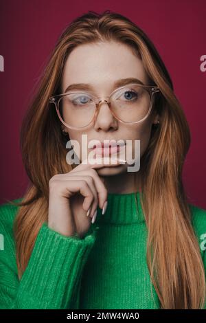 Nahaufnahme einer attraktiven Frau, die das Kinn berührt und eine Brille trägt, die auf purpurnem Hintergrund isoliert aussieht Stockfoto