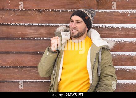 Ein junger Mann, der warme Kleidung an einer Holzwand trägt. Winterurlaub Stockfoto