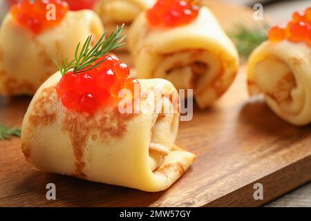 Leckere dünne Pfannkuchen mit rotem Kaviar auf Holzbrett, Nahaufnahme Stockfoto