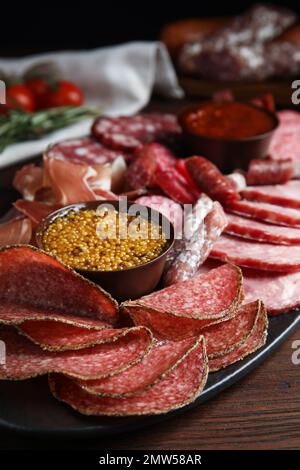 Verschiedene Wurstsorten mit Senf, serviert auf einem Holztisch, Nahaufnahme Stockfoto