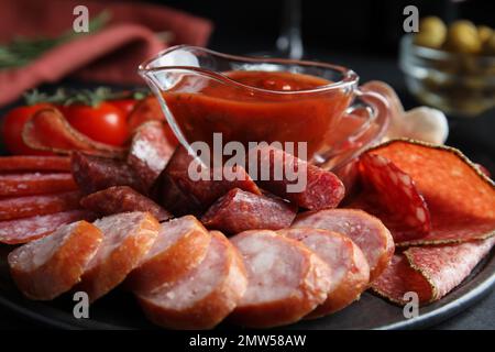 Verschiedene Wurstsorten mit Soße, serviert auf schwarzem Tisch, Nahaufnahme Stockfoto
